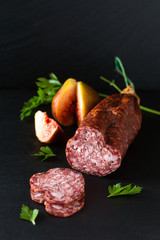 Food concept dried cured sausage on black slate board with copy space