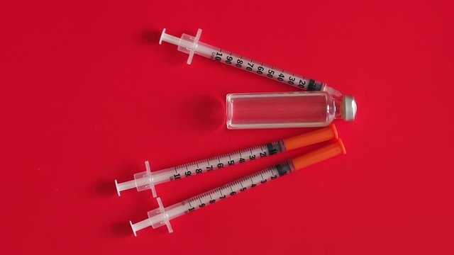 Vial with insulin hormone and single use insulin syringes (pens) lying near the ampule. One syringe needle without cap. Set for diabetic problem. Red background.