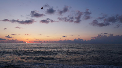 Parasailing in blue sea during orange evening sundown on horizon, beautiful scenery of tranquil seascape in summer evening twilights. Tourists on a parachute over the sea. Sunset paradise 