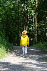 A girl in a bright yellow hoodie with a hat is walking along a path in the forest.