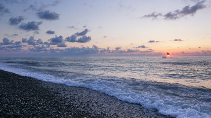 Parasailing in blue sea during orange evening sundown on horizon, beautiful scenery of tranquil seascape in summer evening twilights. Tourists on a parachute over the sea. Sunset paradise 