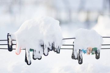 Colorful clips for washing laundry covered with snow on strip rope outdoor. Winter housework...