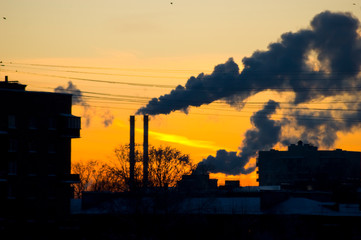 Silhouette of a factory on a sunset background. The environmental issue is environmental pollution. Smoking stacks of a factory.
