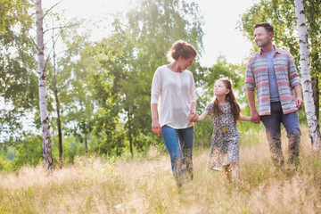 Fototapeta premium Loving young caucasian family walking across woods all holding hands