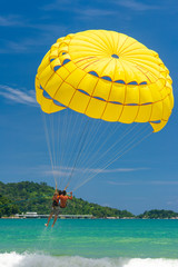 Parasailing is a popular water sport in Patong Beach, Thailand. People flying on colorful parachute towed by speed boat with a clear blue sky in the background. Parasailing water amusement.
