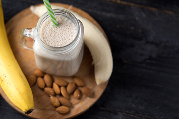 Fresh banana smoothie on a wooden table in a jar . With oatmeal and almonds