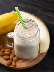 Fresh banana smoothie on a wooden table in a jar . With oatmeal and almonds