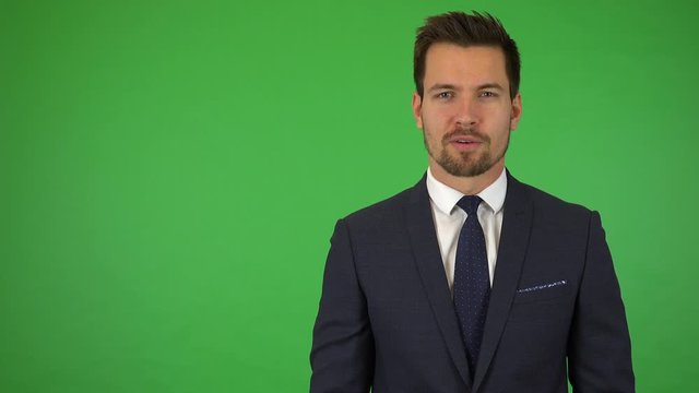 A young handsome businessman talks to the camera with a mild smile - green screen studio