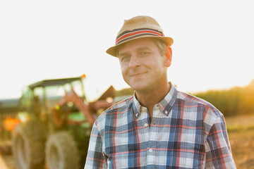 Smiling mature farmer wearing hat while standing against tractor in field
