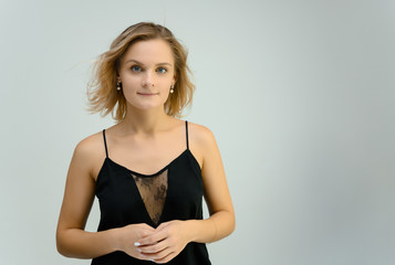 Photo studio portrait of a cute blonde young woman girl in a black blouse on a white background. He stands right in front of the camera, explains with emotion.