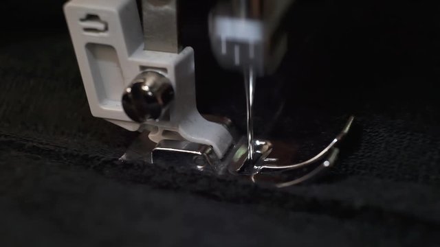 Slow motion shot of the process of sewing black fabric on the sewing machine. Close-up of sewing machine needle slowly moves up and down. The tailor sews black fabric on the sewing workshop