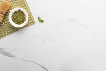 top view of green matcha tea powder and whisk on white table