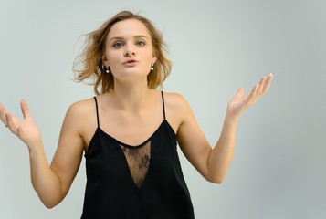 Naklejka na ściany i meble Photo studio portrait of a cute blonde young woman girl in a black blouse on a white background. He stands right in front of the camera, explains with emotion.