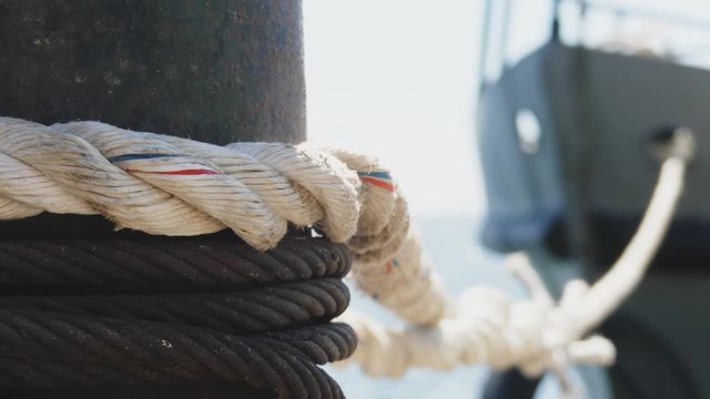 Close-up nautical knot rope tied around stake on boat or ship, boat mooring rope. Marine rope on the ship. The ship leaves the port.  Lighthouse. Mooring rope. Ship in the harbor.