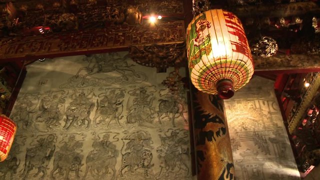 Close-up low-angle panning shot of a glowing traditional Chinese lantern hanging on the ceiling. On the wall are grey coloured murals, Leong San Tong Khoo Kongsi (clan house), Georgetown, Penang