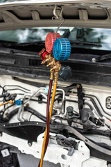 Checking car air conditioning system: refrigerant recharge, connecting pipes for freon refill, leak detection by manometer gauge. Car service by an auto mechanic in garage, fixing a car air condition.