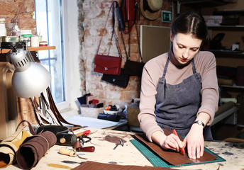 young brunette woman works in a bag making studio, cuts out details - obrazy, fototapety, plakaty