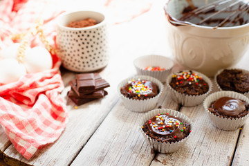 Сhocolate muffins with colorful pastry topping on a wooden table with ingredients