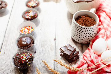 Сhocolate muffins with colorful pastry topping on a wooden table with ingredients