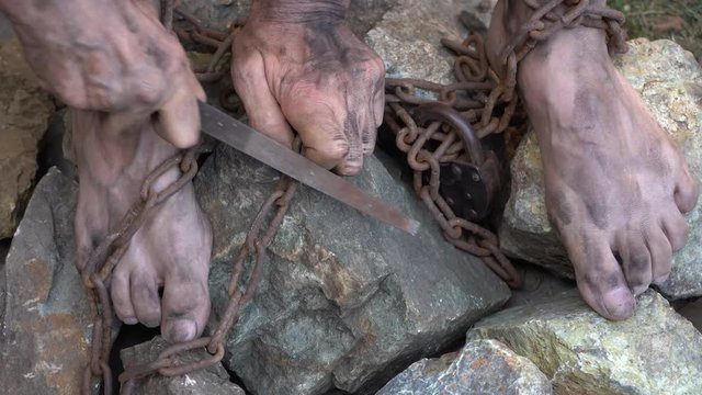 Hands and feet of a slave entangled in iron chains. An attempt to break free from slavery. The symbol of slave labor. Hands in chains.