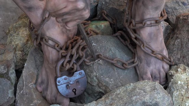 Hands and feet of a slave entangled in iron chains. An attempt to break free from slavery. The symbol of slave labor. Hands in chains.