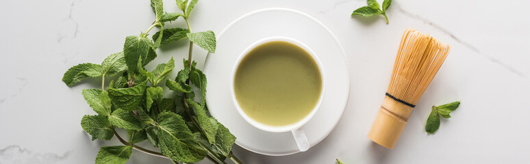 top view of green matcha tea with mint and whisk on white table