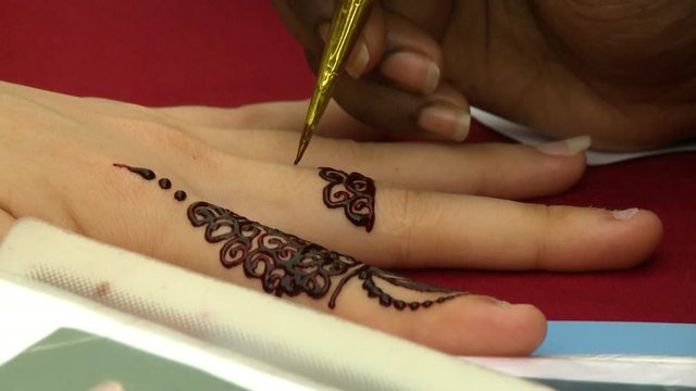 Extreme close-up low-angle still shot of a henna artist using his hand to paint patterns on a lady's fingers, George Town, Penang, Malaysia