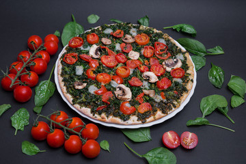 Pizza vegana con espinacas, tomates cherry y champiñones sobre fondo negro.
