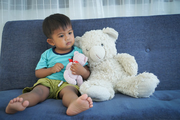 Cute little boy sitting on the sofa with teddy bear