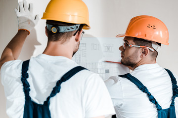 selective focus of architect in helmet looking at blueprint near coworker