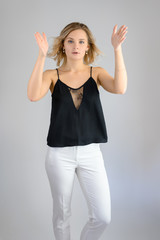 Fototapeta na wymiar Full length studio portrait photo of a cute young blonde woman girl in a black blouse and white pants on a white background. He stands right in front of the camera, explains with emotion.