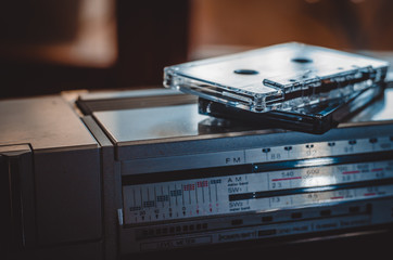 Two analog audio cassettes on top of a cassette player. Close-up. Eye level shooting. Soft focus.