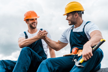 happy handymen holding hands while smiling against sky