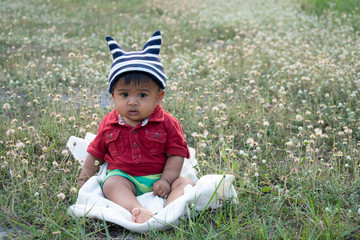 Cute happy little asian baby boy sitting at white flower garden