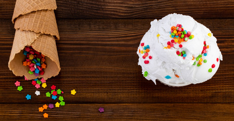 plate of vanilla ice cream scoop swith sprinkles and waffle cones on wooden background with copy space