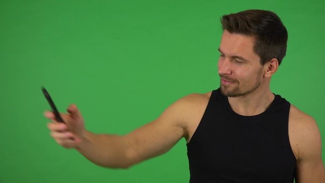 A young handsome athlete takes selfies with a smartphone - green screen studio