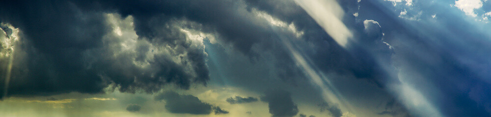 panorama of cloudy sky with streaks of sun rays, dark rain clouds announcing the change of weather