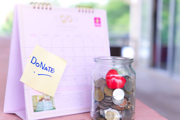 Coins in glass jar with DONATE word label on calendar for giving and donation concept  S