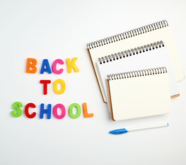inscription back to school from multi-colored plastic letters and a stack of notebooks