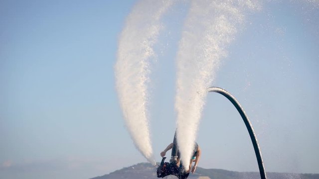 Flyboarding is a new extreme water sport. Athletic man performs tricks in flight. Spectacular sports coups and turns.
