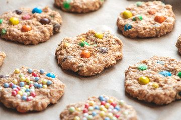 Raw cookie dough with colorful chocolate balls on a baking tray close-up.
