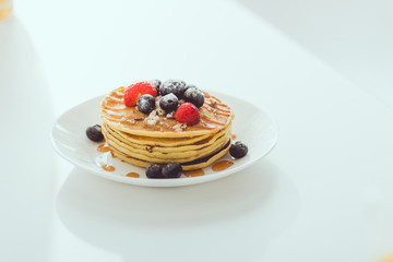 plate of pancakes with blueberries and strawberries on white table
