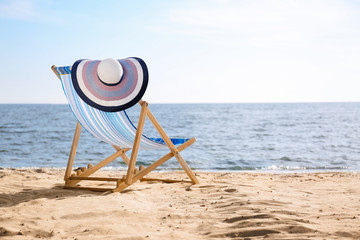 Lounger and hat on sand near sea, space for text. Beach objects