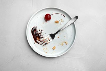 Dirty plate with food leftovers, fork and canned cherry on grey background, top view