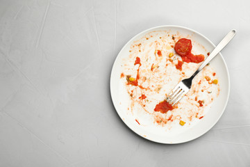 Dirty plate with food leftovers and fork on grey background, top view. Space for text