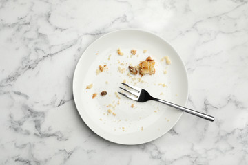 Dirty plate with food leftovers and fork on marble background, top view