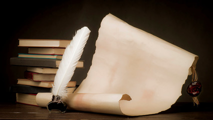 Scroll of parchment and inkwell with a pen on the background of the stack of books