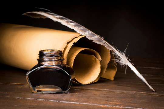 Parchment scrolls and inkwell with a pen on the background of boards