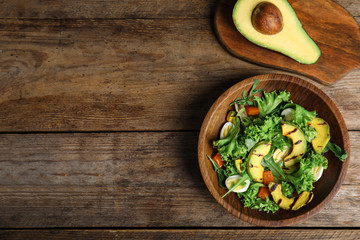 Delicious avocado salad with boiled eggs in bowl on wooden table, flat lay. Space for text