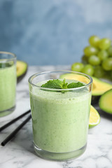 Glass of tasty avocado smoothie with mint on marble table